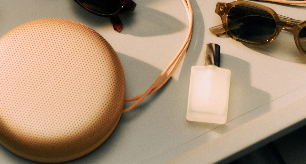 Beosound A1 3rd Gen aplikacja Bang & Olufsen ustawienia dźwięku, głośnik leżący na biurku z okularami oraz fiolką perfum