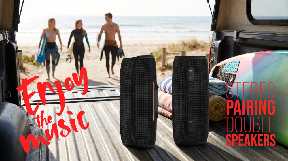 Na obrazie widać dwa czarne głośniki mobilne ustawione na otwartej klapie bagażnika samochodu, z widokiem na plażę i ocean. Tekst na obrazie: \'Enjoy the music\' oraz \'STEREO PAIRING DOUBLE SPEAKERS\'.