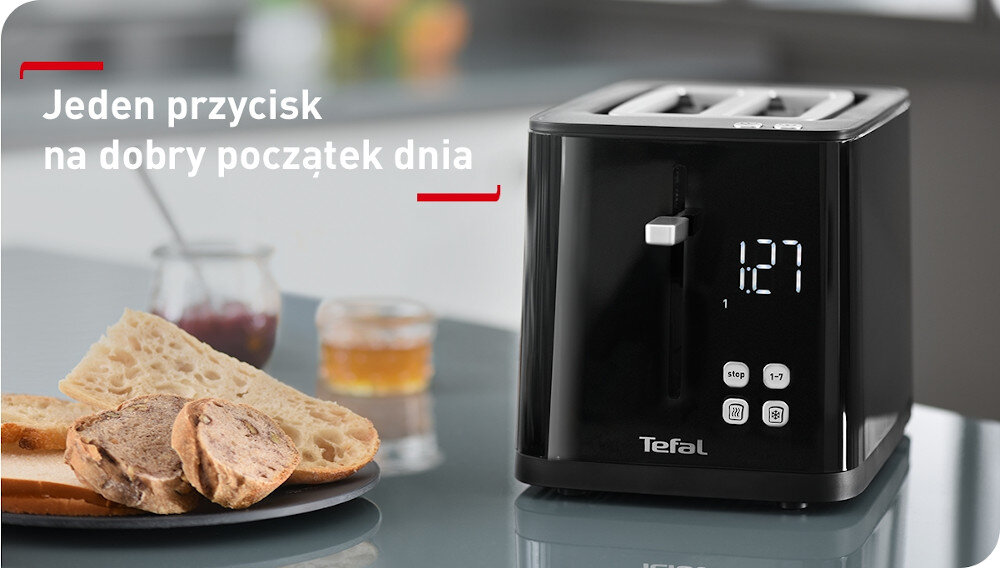 Czarny toster z wyświetlaczem cyfrowym pokazującym \'1:27\' oraz trzema przyciskami funkcyjnymi. Obok tostera leżą kromki chleba i słoik z dżemem, a na obrazie widnieje tekst: \'Jeden przycisk na dobry początek dnia\'.