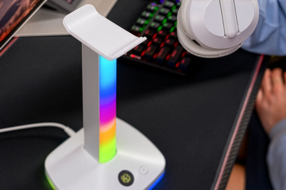 MAD DOG HPS800W Biały stojak na słuchawki MAD DOG z tęczowym podświetleniem RGB. Widoczna podstawa z przyciskami oraz kawałek klawiatury w tle