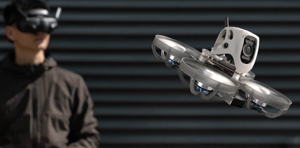 Dron BETAFPV Meteor65 Pro O4 Dron w locie na tle rozmytej sylwetki osoby w goglach FPV stojącej przed ciemną ścianą