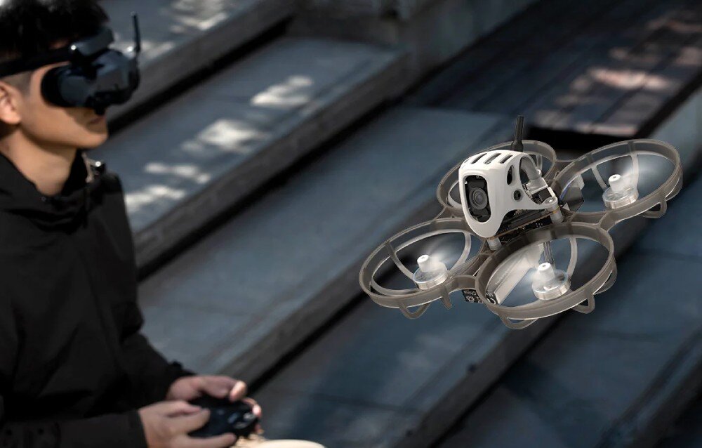 Dron BETAFPV Meteor75 Pro O4 Dron unoszący się w powietrzu na pierwszym planie, za którym widać nieostrą sylwetkę osoby w goglach do podglądu obrazu