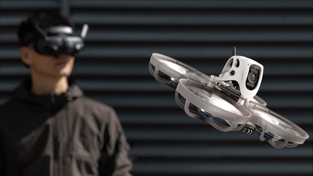 Dron BETAFPV Meteor75 Pro O4 Dron w locie ujęty z bliska z widocznym w tle operatorem trzymającym w dłoniach aparaturę sterującą