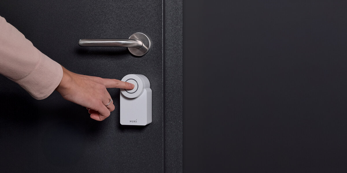 Zamek Nuki Smart Lock Go, akcesoria, smart lock, aplikacje, integracja, palec dłoni naciska na zamek nuki zamontowany do drzwi
