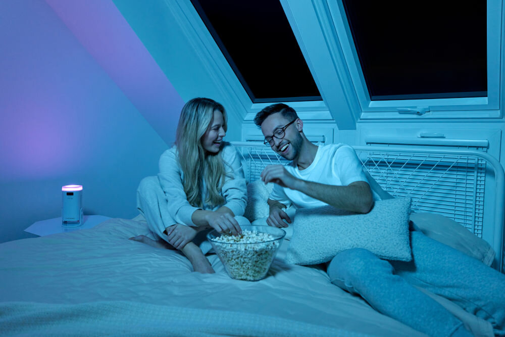 Projektor OVERMAX Multipic Veer - Wysoka jakość obrazu, projektor stojący na nóżce na sztorc, ludzie leżący na łóżku, jedzący popcorn, oglądający wyświetlany obraz przez projektor