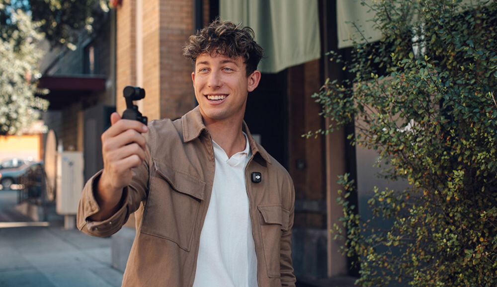 Nadajnik DJI Mic 3 mężczyzna nagrywający na mieście za pomocą osmo pocket i używający DJI Mic 3 nadajnik i odbiornik z technologią DJI OsmoAudio™ do bezpośredniego połączenia z Osmo i wsparciem Bluetooth kompatybilność porty