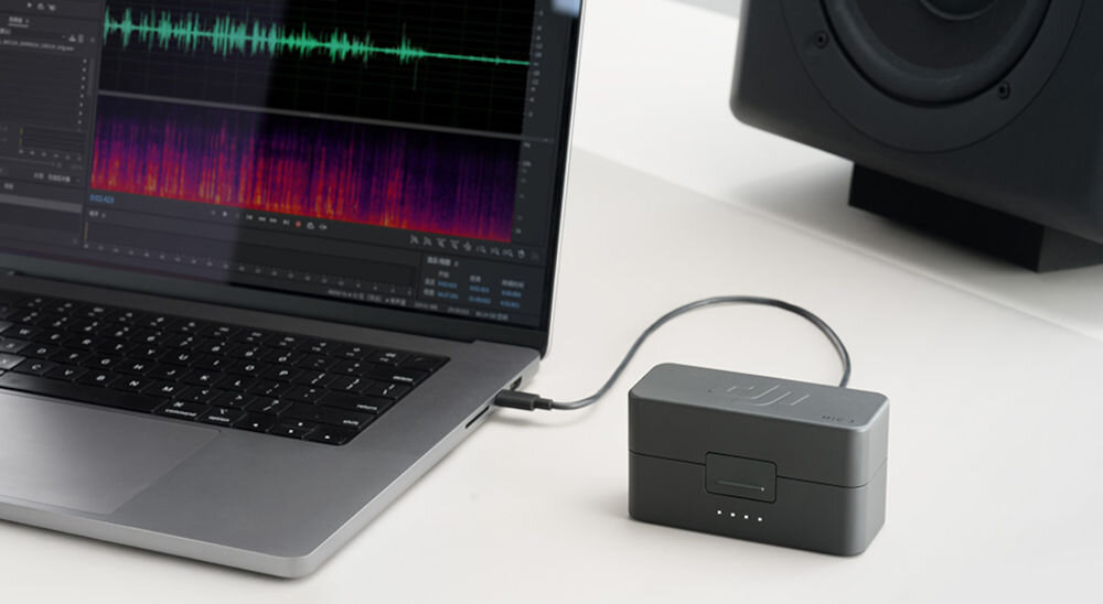 Nadajnik DJI Mic 3 etui podłączone do laptopa na laptopie widoczna ścieżka dźwiękowa w programie edytującym obok głośnik system z funkcją wewnętrznego nagrywania dwóch ścieżek audio w 32-bitowym formacie float szeroki zakres dynamiki usprawnienie procesu edycji