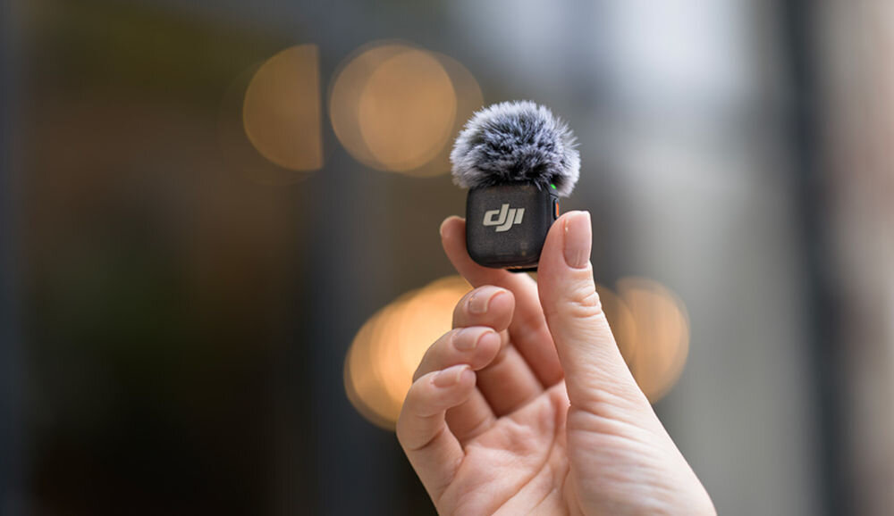 Nadajnik DJI Mic 3 prezentacja nadajnika w ręce rozmazane tło vlogi podcasty reportaże rozmowy grupowe mikrofon bezprzewodowy 4TX 8RX z 4 kanałami, adaptacyjnym wzmocnieniem i zapisem 32-bit float
