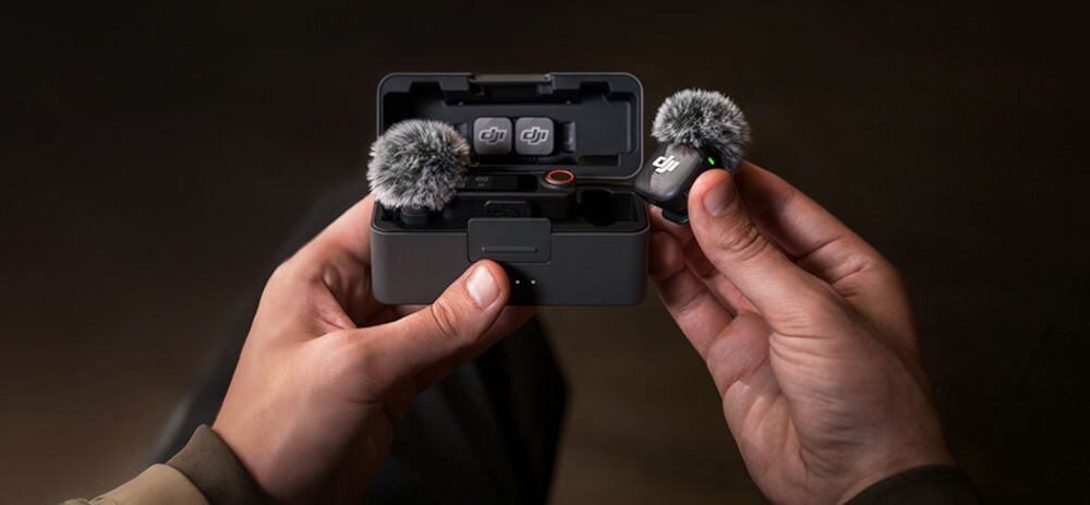 System bezprzewodowy DJI Mic 3 (2 TX + 1 RX + Etui ładujące) prezentacja etui trzymanego w rękach w środku nadajnik i odbiornik jeden mikrofon trzymany w dłoni na ciemnym tle Akcesoria DJI Mic 3: osłony przeciwwietrzne, adapter Lightning oraz HDMI Camera Adapter do Sony nagrywanie cyfrowego dźwięku zapis 4 osobnych ścieżek