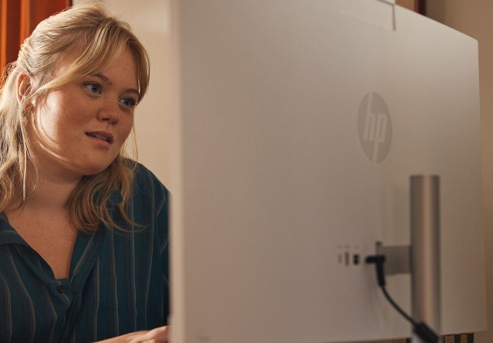 Komputer HP All-in-One 27-cr0232nw Osoba patrząca na ekran komputera, widoczny tył urządzenia z logo producenta i podłączonym przewodem, podzespoły, procesor, pamięć, dysk