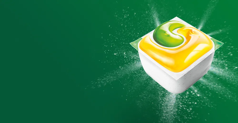 Trójkolorowa kapsułka do zmywarki Fairy na zielonym tle z rozpryskiem detergentu.