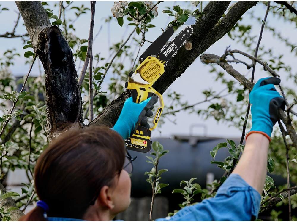 Osoba w niebieskich rękawicach używa żółtej piły łańcuchowej do przycinania gałęzi drzewa. Na pile widoczne jest logo \'IMOUM\'.