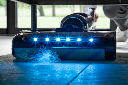 Bezprzewodowy odkurzacz X-CLEAN 7 z podświetleniem LED zbiera kurz spod mebla.