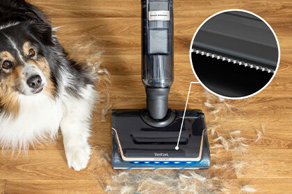 Bezprzewodowy odkurzacz X-CLEAN 7 z diodami LED zbiera sierść psa z drewnianej podłogi, zbliżenie na grzebień z ząbkami.