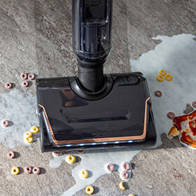 Kobieta odkurza pod łóżkiem X-CLEAN 7. Kadr z góry: odkurzacz X-CLEAN 7 zbiera rozlane mleko i płatki śniadaniowe.