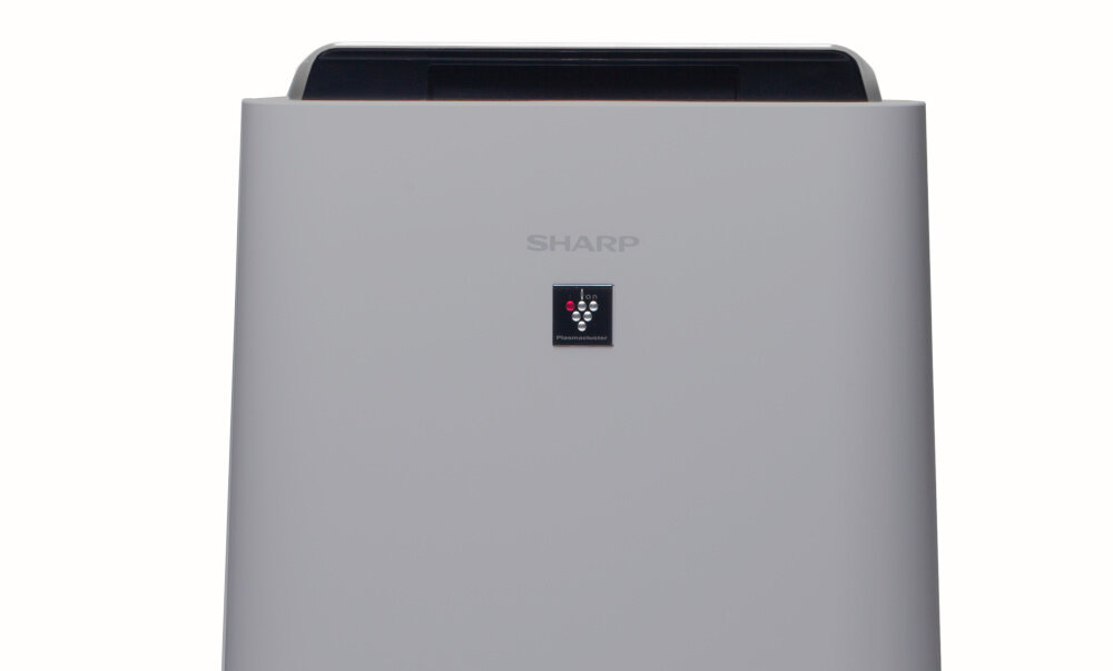 Na obrazie widoczny jest oczyszczacz powietrza w kolorze białym z logo SHARP na górnej części. Poniżej znajduje się panel z kilkoma ikonami i wskaźnikami świetlnymi.