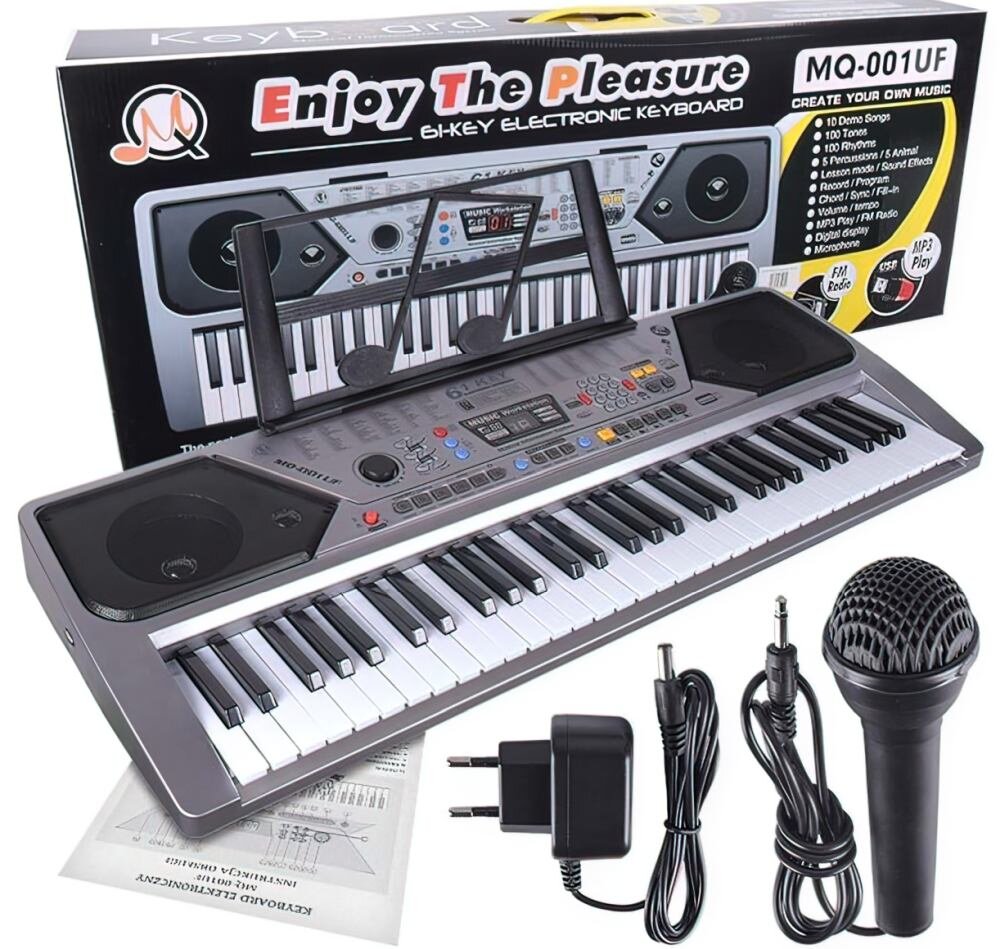 Na obrazie znajduje się elektroniczny keyboard z 61 klawiszami, mikrofon, zasilacz i przewody. W tle widoczny jest karton z napisem \'Enjoy The Pleasure\' oraz \'MQ-001UF\'.
