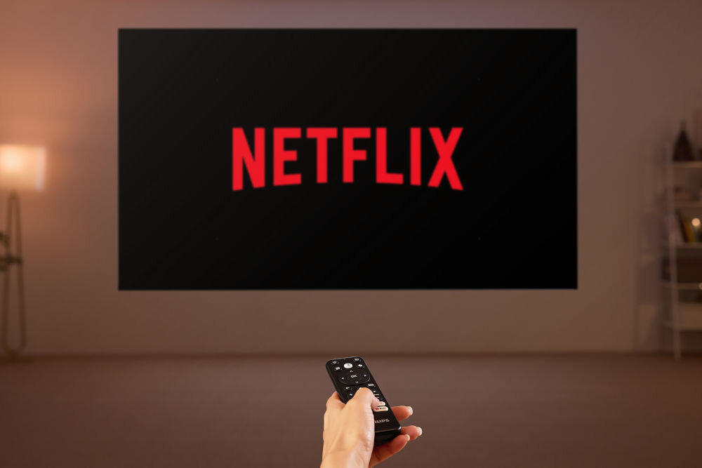 Projektor PHILIPS GamePix 800 funkcje smart Bluetooth Google TV, obraz wyświetlany na ścianie, ręka trzymająca pilota