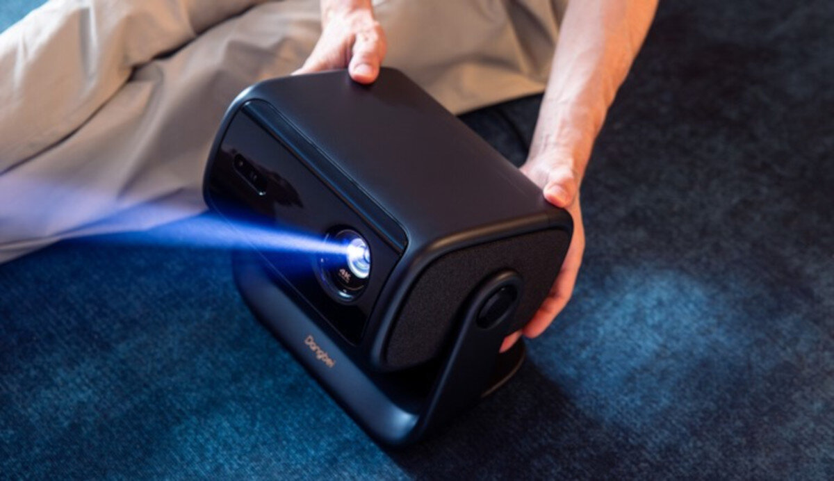 Projektor DANGBEI MP1 Max — kino domowe, realistyczny obraz, wysoka jasność ISO, tri-laser LED hybryda, projektor stojący na podłodze, osoba ustawiająca projektor