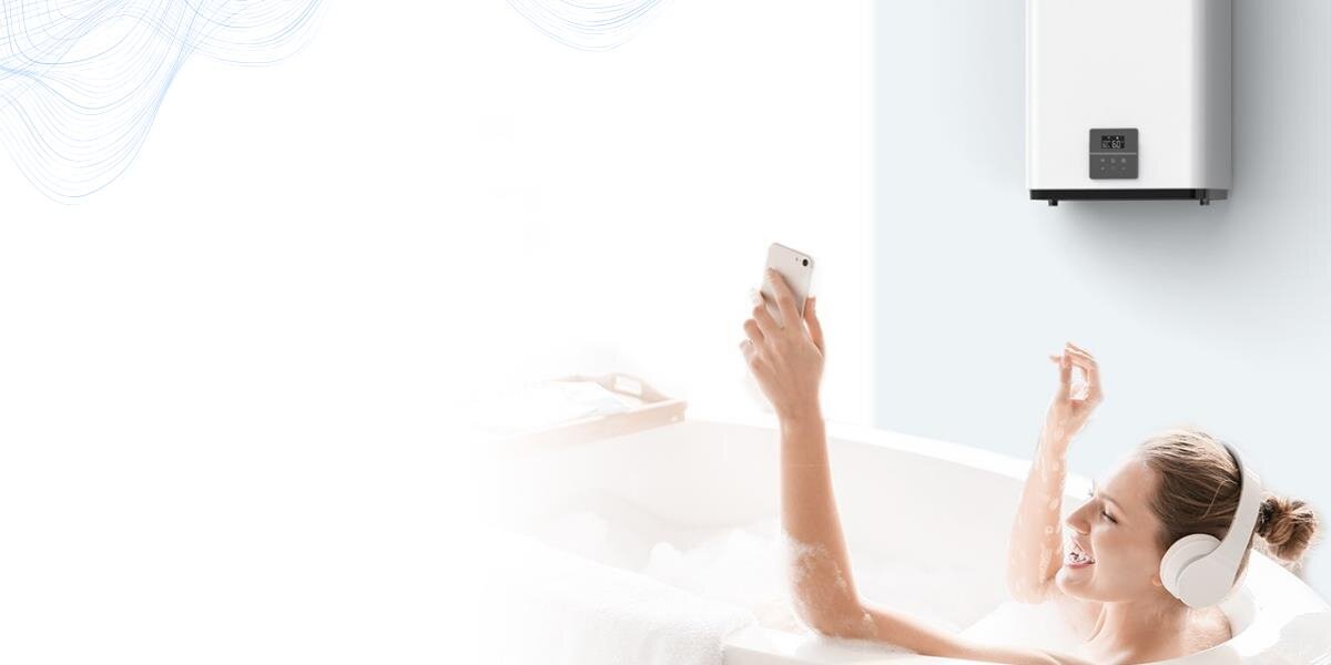 Osoba relaksuje się w wannie, trzymając telefon i nosząc słuchawki. Na ścianie zamontowany jest biały bojler elektryczny z wyświetlaczem cyfrowym.
