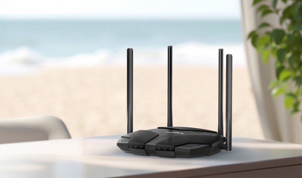 Router MERCUSYS MB235-4G Czarny router z czterema antenami ustawiony na stole na tle rozmytego widoku plaży i morza, opis