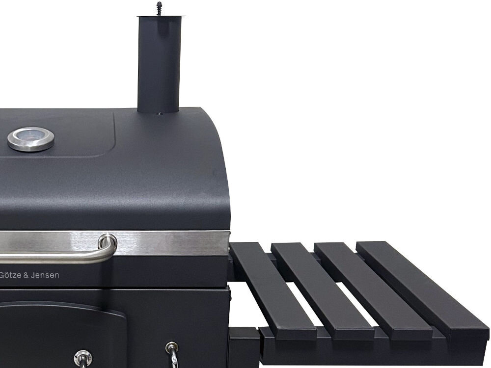 Grill węglowy GÖTZE & JENSEN GG710 z kominem 56.5 x 41.8 cm Zbliżenie na górną część czarnego grilla węglowego z wbudowanym termometrem, kominem i boczną półką z listew.