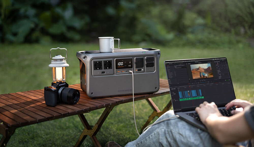 Stacja zasilania DJI 1000 V2 1024Wh Bank energii, usb, porty, W, moc, AC, gniazda, osoba pracuje na podłączonym do laptopa zasilacza która stoi na stole