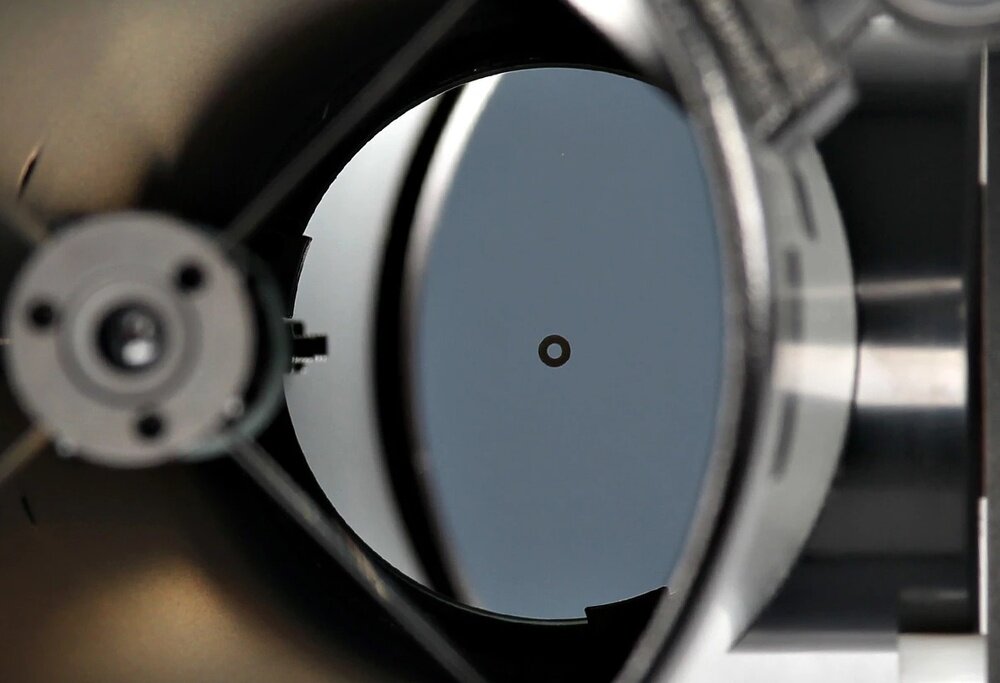 Zbliżenie na wnętrze teleskopu z widocznym okrągłym lustrem i centralnym punktem. Elementy konstrukcyjne są metaliczne i ciemne.