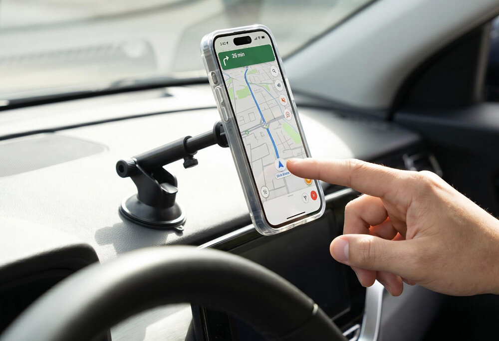 Telefon zamocowany jest na uchwycie samochodowym na desce rozdzielczej, wyświetlając mapę z trasą. Osoba dotyka ekranu telefonu.