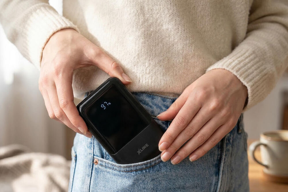 Osoba wkłada czarny powerbank z logo \'XLINE\' do kieszeni spodni. Na wyświetlaczu powerbanka widoczny jest napis \'97%\'.