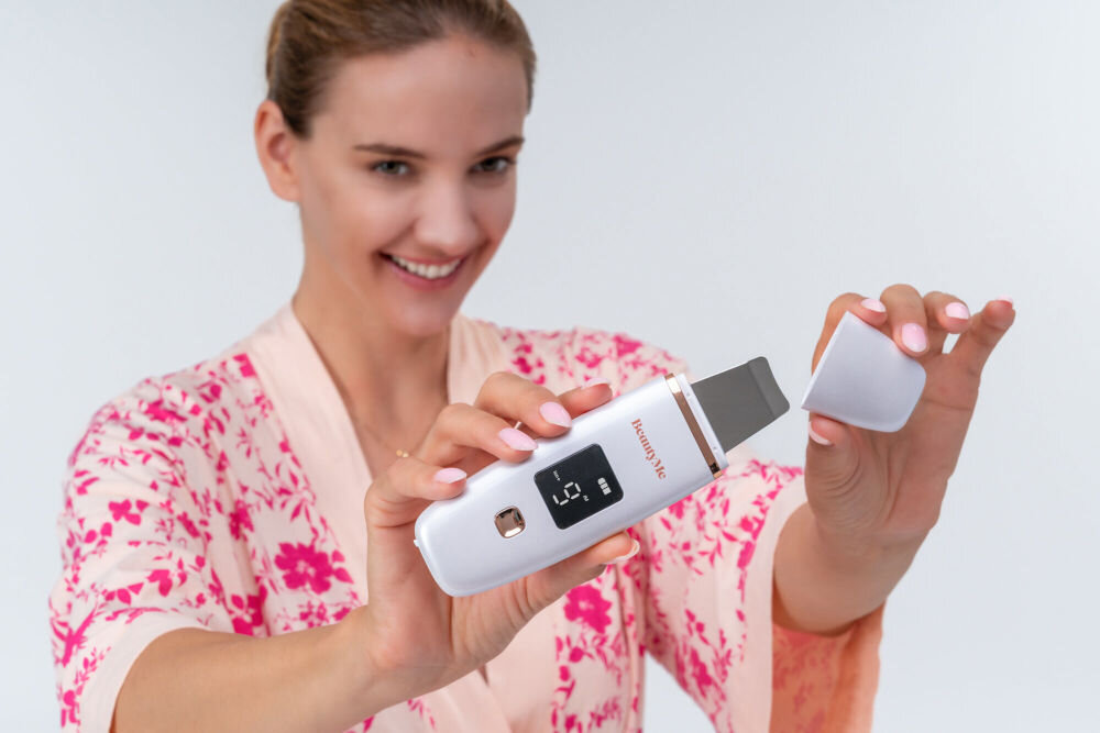 Osoba trzyma urządzenie do peelingu kawitacyjnego BEAUTYME Skin Protect SSC501 24 kHz z wyświetlaczem i metalową końcówką. Na urządzeniu widoczne jest logo \'beautyMe\'.