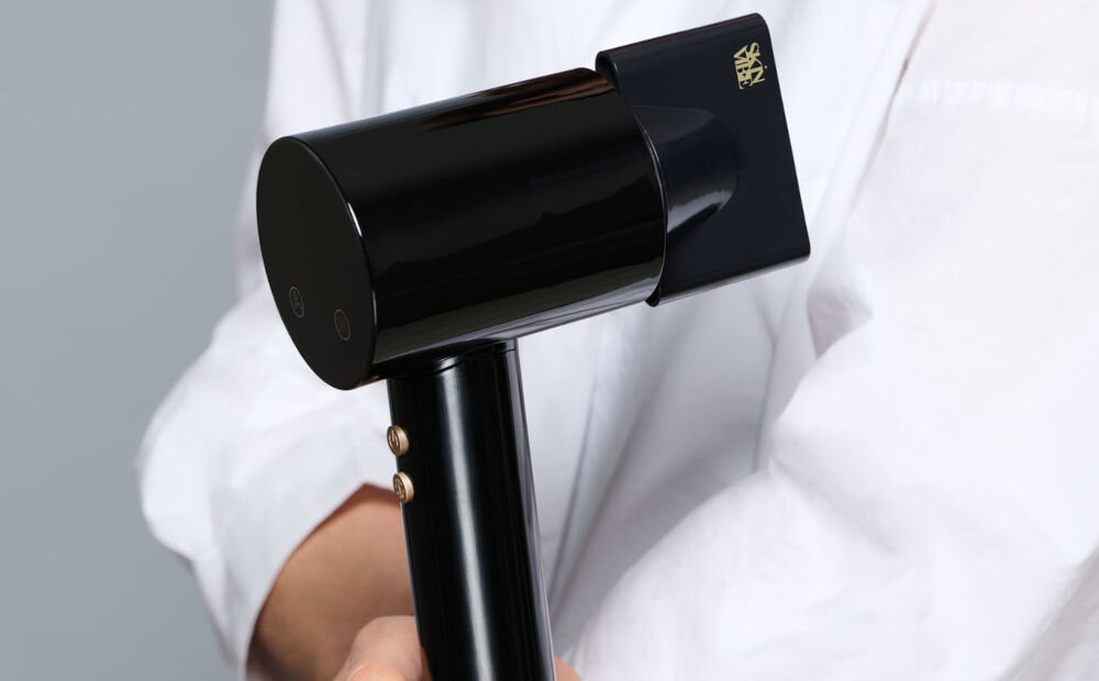 Suszarka SKINVIBE Libra Airloom SV-002BK Czarny 1500W osoba trzyma w ręce czarną suszarkę przyczepiona końcówka złote przyciski system jonizacji naturalna harmonia miękkie w dotyku włosy jedwabisty blask sprężystość wymagające warunki funkcjonalność troska o piękno olśniewający wygląd 