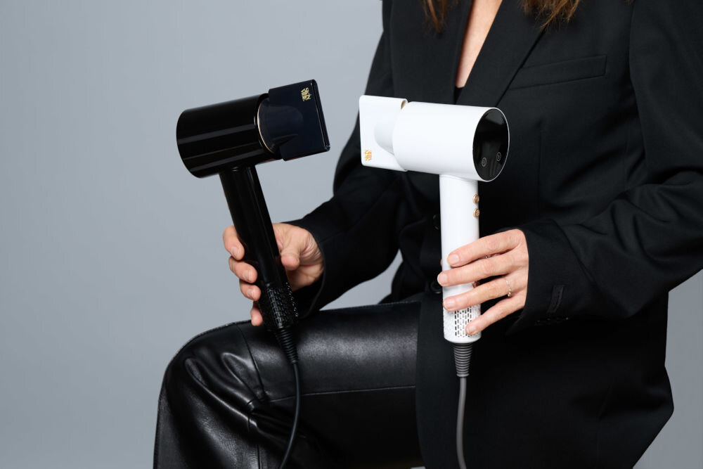 Suszarka SKINVIBE Libra Airloom SV-002BK Czarny 1500W kobieta z brązowymi włosami siedzi na pomarańczowym krześle trzyma w reku czarną suszarkę  z koncentratorem elegancki design funkcjonalność dotykowy ekran LCD precyzyjna regulacja temperatury i siły nawiewu cztery ustawienia temperatury 50, 70 i 90 stopni zimny nawiew technologia jonizacji 200 milionów jonów ujemnych lekka konstrukcja ergonomiczny uchwyt wygoda przewód 2,7 m zwiększona swoboda ruchów  