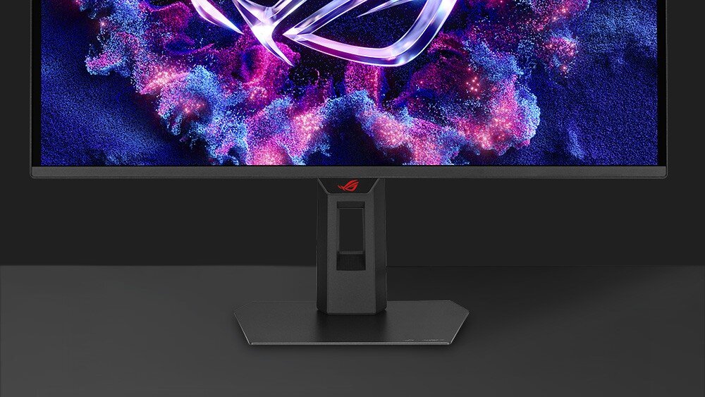 Monitor ASUS ROG Strix XG27AQDPG Zbliżenie na dolną część monitora oraz czarną, płaską podstawę o szerokim profilu, na ekranie widoczny jest fragment kolorowej grafiki, a na obudowie pod panelem znajduje się małe, czerwone logo, wygląd, ramka, podstawa