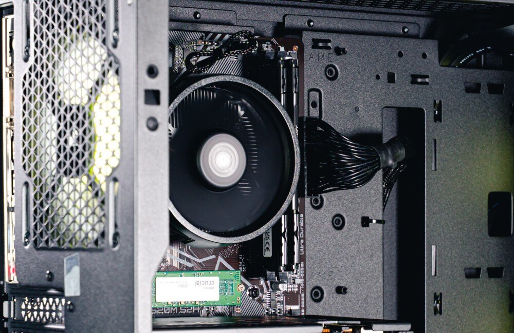 Komputer OPTIMUS E-Sport GA520T-CR10 Zbliżenie na podzespoły zamontowane na płycie głównej, w tym okrągłe chłodzenie procesora, dwa moduły pamięci RAM oraz dysk SSD M.2 z zieloną naklejką, pamięć RAM, taktowanie, dysk, pojemność