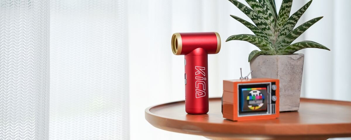 Dmuchawa wielofunkcyjna KICA Jetfan 2S Czerwona, Czerwona dmuchawa Jetfan 2Sna okrągłym drewnianym stoliku. Obok kwiatek w donicy i mały prlowski telewizorek, turbo, 30% większy, ergonomiczny, Jetfan2