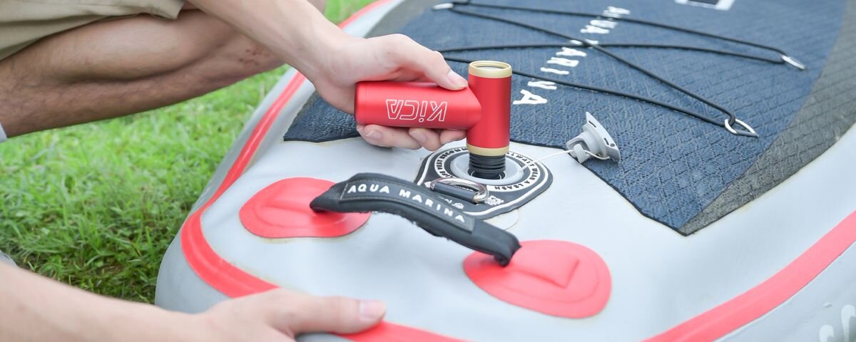 Dmuchawa wielofunkcyjna KICA Jetfan 2S Czerwona, Męska dłoń pompuje czerwoną dmuchawą KiCa Jetfan 2S deskę typu SUP, leżącą na trawie, suwak, bezstopniowy, precyzyjny, kurz