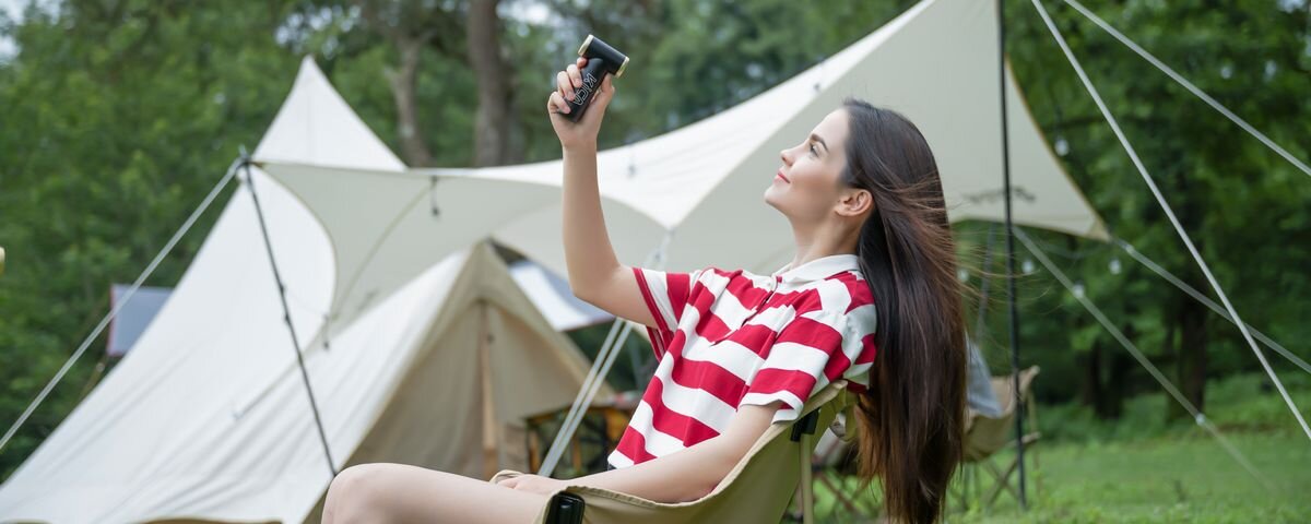 Dmuchawa wielofunkcyjna KICA Jetfan 2S Czerwona, Kobieta siedząca przed namiotem na campingu chłodzi się czarną dmuchawą wielofunkcyjną KiCA Jetfan 2S, 1100mAh, 4,5h, USB-C, 3 minuty