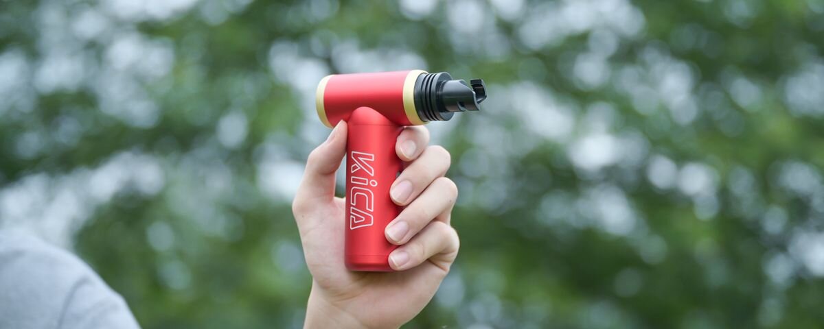 Dmuchawa wielofunkcyjna KICA Jetfan 2S Zielony, Czerwona dmuchawa wielofunkcyjna KiCA Jetfan 2S z końcówką do pompowania, trzymana w dłoni na tle rozmazanej zieleni, wąskie, klawiatura, materac, ponton