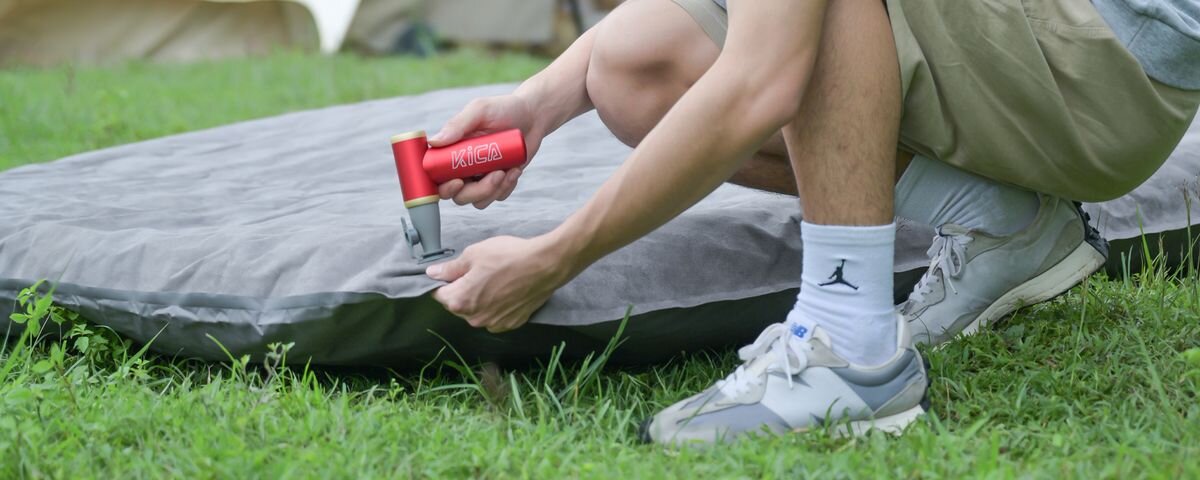 Dmuchawa wielofunkcyjna KICA Jetfan 2S Zielony, Męska dłoń pompuje szary materac leżący na trawie czerwoną dmuchawą wielofunkcyjną KiCA Jetfan 2S, aluminum, kolory, biuro, zarysowania