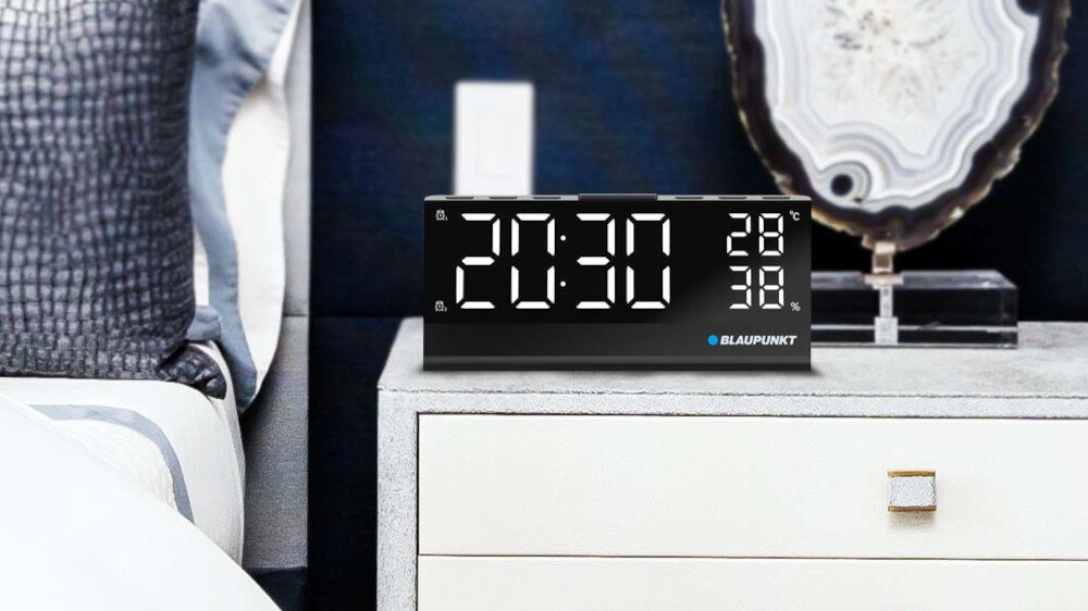 Na szafce nocnej stoi czarny radiobudzik z dużym wyświetlaczem pokazującym godzinę 20:30 oraz temperaturę 28°C i 38%. Widoczne jest logo BLAUPUNKT.