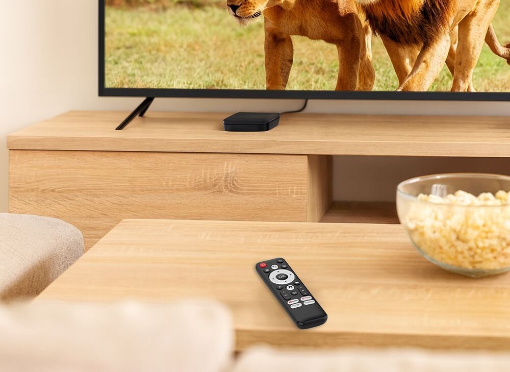 Odtwarzacz multimedialny 4K TRACER TV Box centrum domowej rozrywki streaming aplikacje VOD kompaktowa obudowa, pilot leżący na stole, urządzenie podłączone do telewizora
