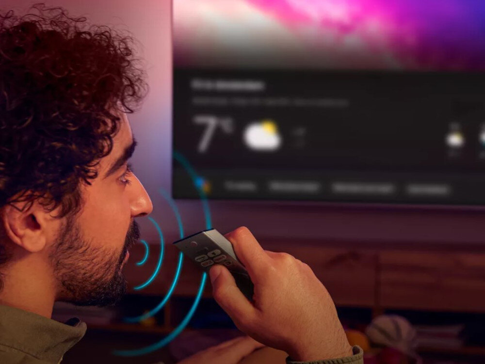 Telewizor PHILIPS 48OLED820 inteligentne sieci Matter Alexa AirPlay, osoba mówiąca do pilota, telewizor zawieszony na ścianie nad szafką