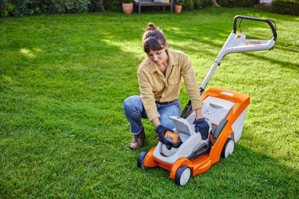 Akumulator STIHL AK 20 4Ah 36V, akumulator, ogród, nożyce, lekki, Osoba w rękawicach wpina akumulator do kosiarki STIHL.
