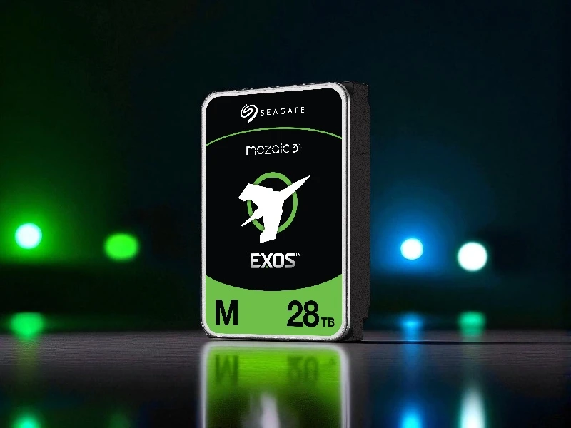 Na obrazie widoczny jest dysk twardy z logo \'SEAGATE\' oraz napisami \'mozaic 3+\', \'EXOS\', \'M\', \'28TB\'. Tło jest ciemne z rozmytymi, kolorowymi światłami.