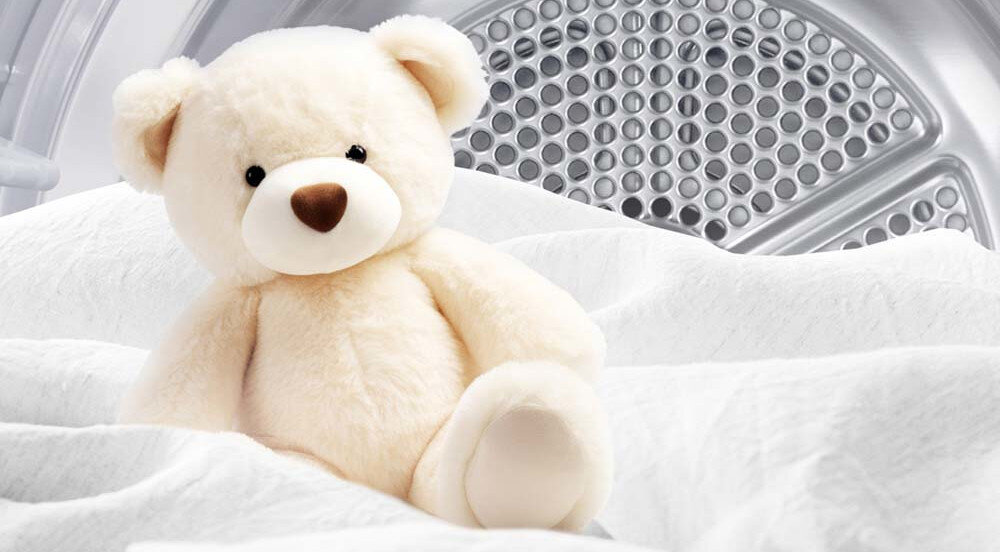 SUSZARKA LG RHX7010TBB Zdjęcie przedstawia pluszowego misia siedzącego na białej tkaninie, na tle wnętrza bębna suszarki. Scena podkreśla delikatność suszenia i bezpieczne warunki nawet dla najbardziej miękkich i wrażliwych materiałów Allergy Care 60°C redukcja alergenów roztocza kurzu higienizacja tkanin czystsze pranie bezpieczne pranie alergicy wrażliwa skóra delikatna skóra pranie dla dzieci higieniczne pranie świeżość ochrona tkanin