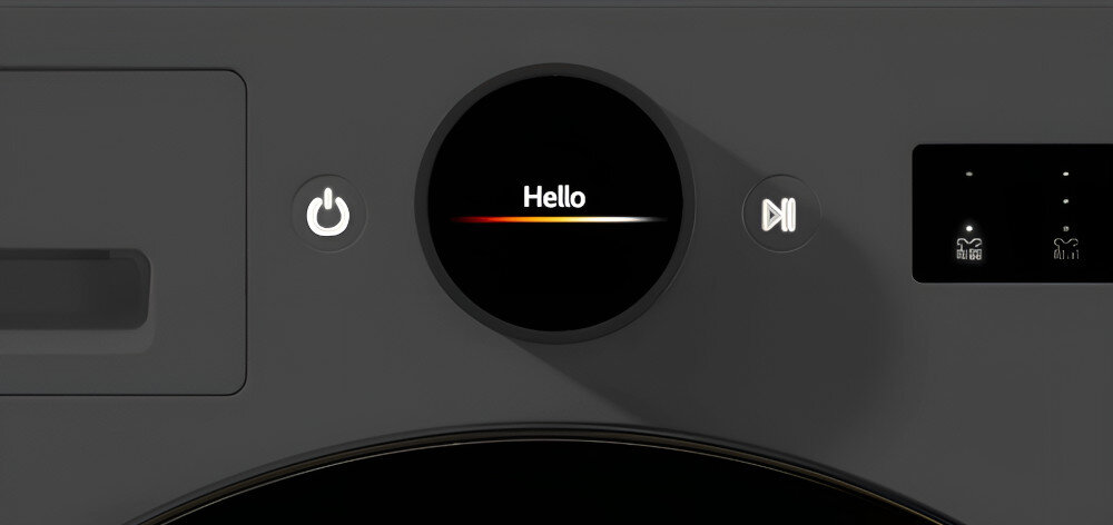 SUSZARKA LG RHX7010TBB Na zdjęciu pokazano zbliżenie na panel sterowania urządzenia. Centralnie widoczny jest okrągły wyświetlacz z napisem „Hello” na ciemnym tle. Po obu stronach ekranu umieszczono ikonę zasilania oraz przycisk start/pauza