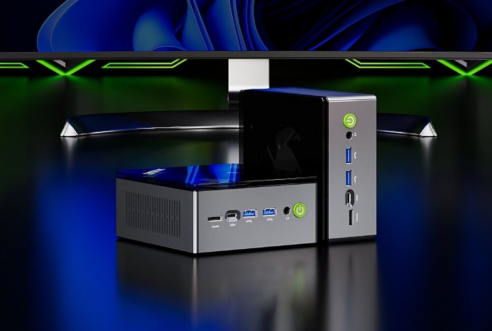 Komputer GMKTEC M7 Dwa miniaturowe komputery stojące na ciemnym biurku przed dużym monitorem, widoczne są porty USB, USB-C, OcuLink, złącze audio oraz przycisk zasilania, opis