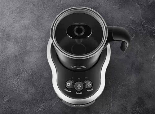 Na obrazie widoczny jest spieniacz do mleka z przezroczystą pokrywką i czarnym uchwytem. Na urządzeniu znajdują się przyciski z ikonami i napisami: \'cold froth\', \'hot froth\', \'warm up\'.