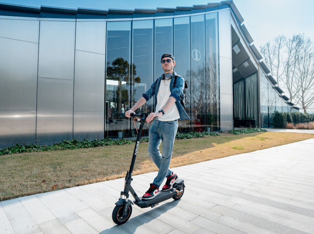 Hulajnoga elektryczna NAVEE GT3 45 km 350W Amortyzacja Czarny 10 cali miasto chodnik budynek osoba jedzie na hulajnodze po chodniku przednie zawieszenie z podwójnym widelcem tylne z podwójnym amortyzatorem komfort i stabilność skuteczniej tłumi drgania i nierówności płynność pewność prowadzenia poprawia przyczepność kół do podłoża